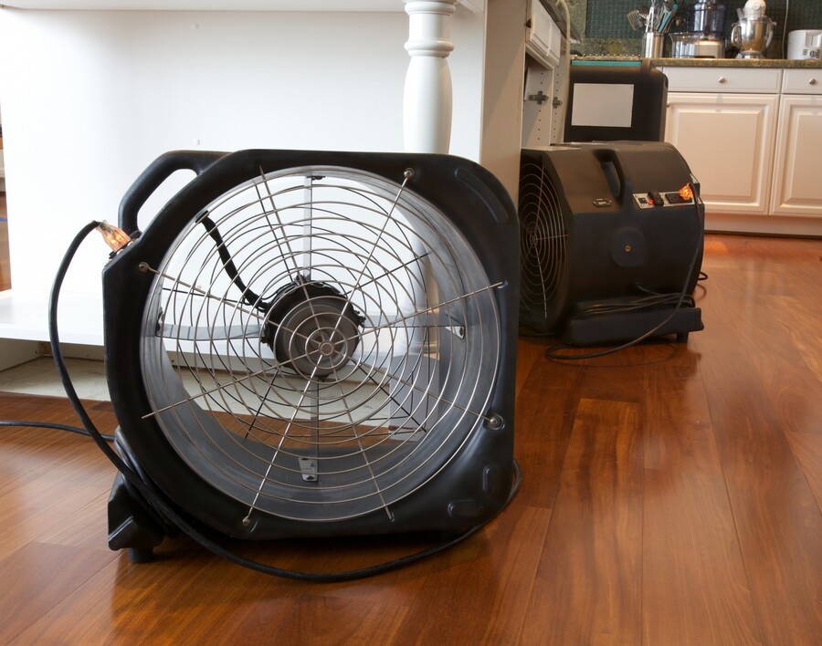 Portable drying fans on hardwood floor in a kitchen, used for water damage dry out services